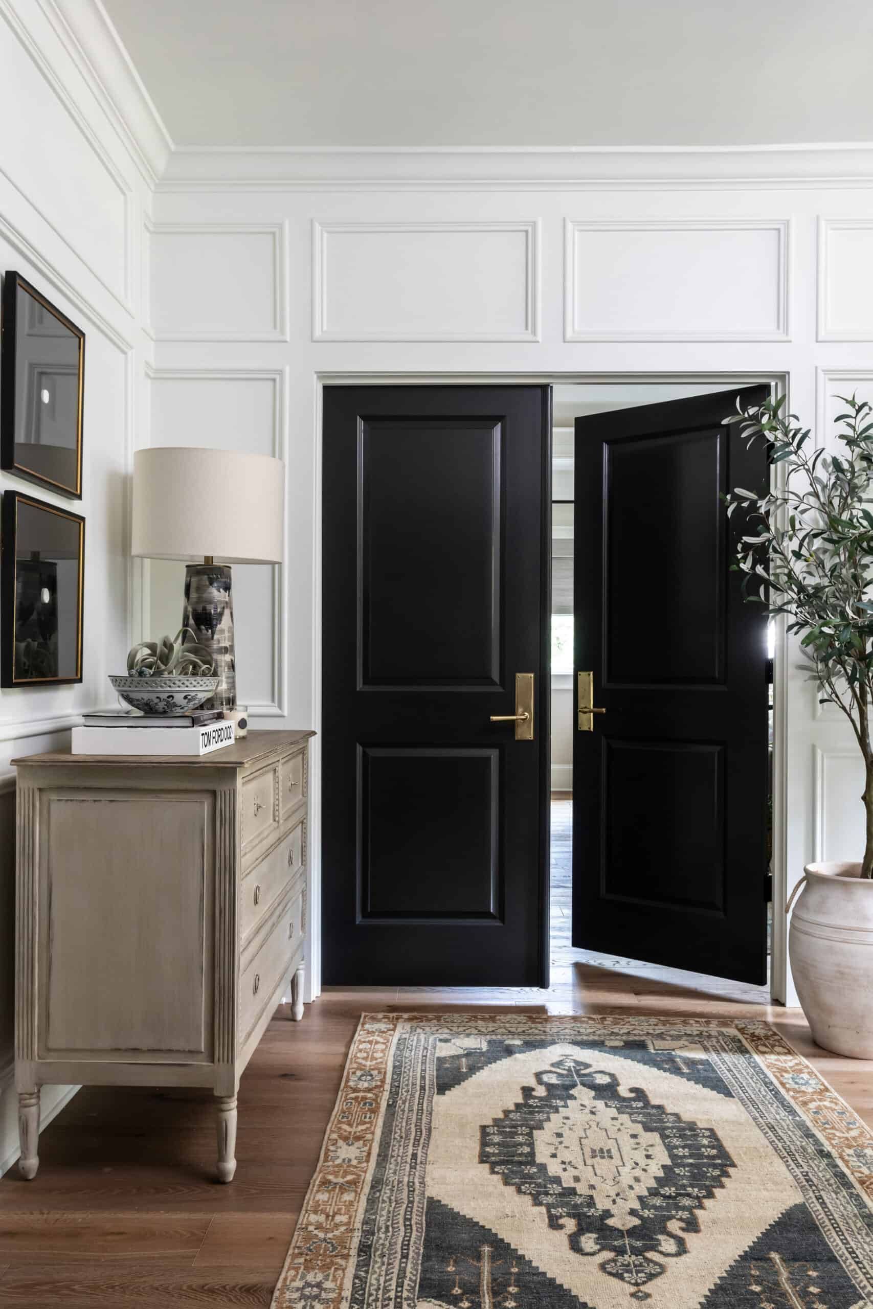 Hallway with double black doors and classic white wall paneling. 